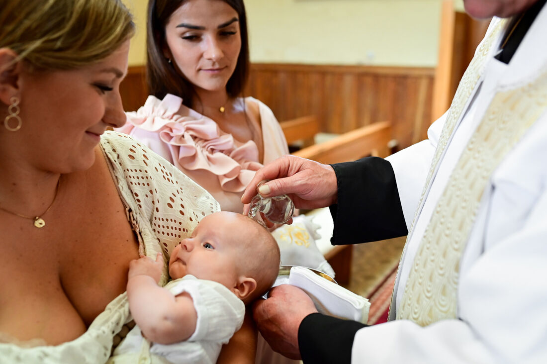 Chrzest święty — ksiądz podczas ceremonii z dzieckiem na rękach mamy
